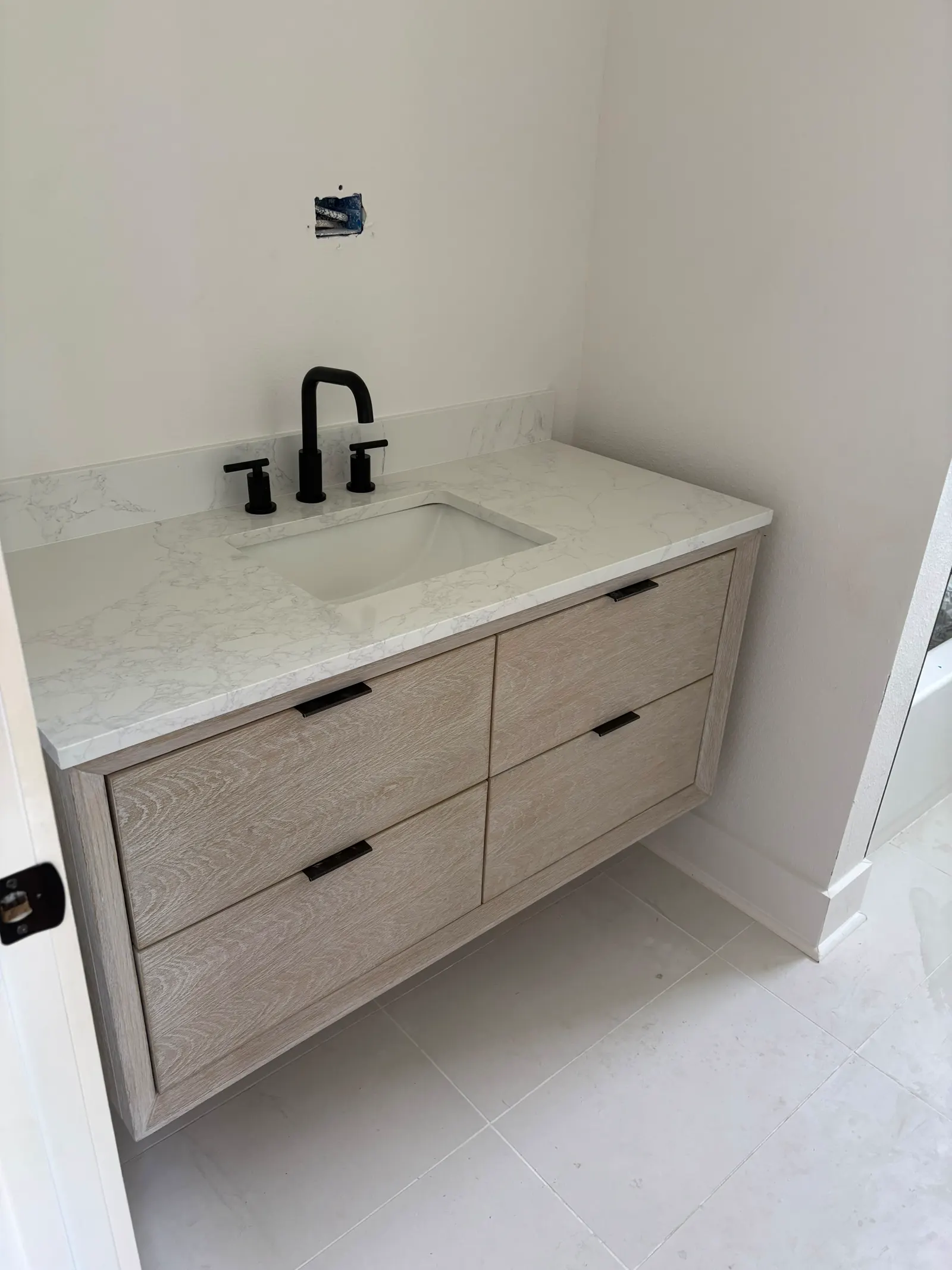 Wood-tone vanity with a light countertop, black faucet and visible bathroom floor tile