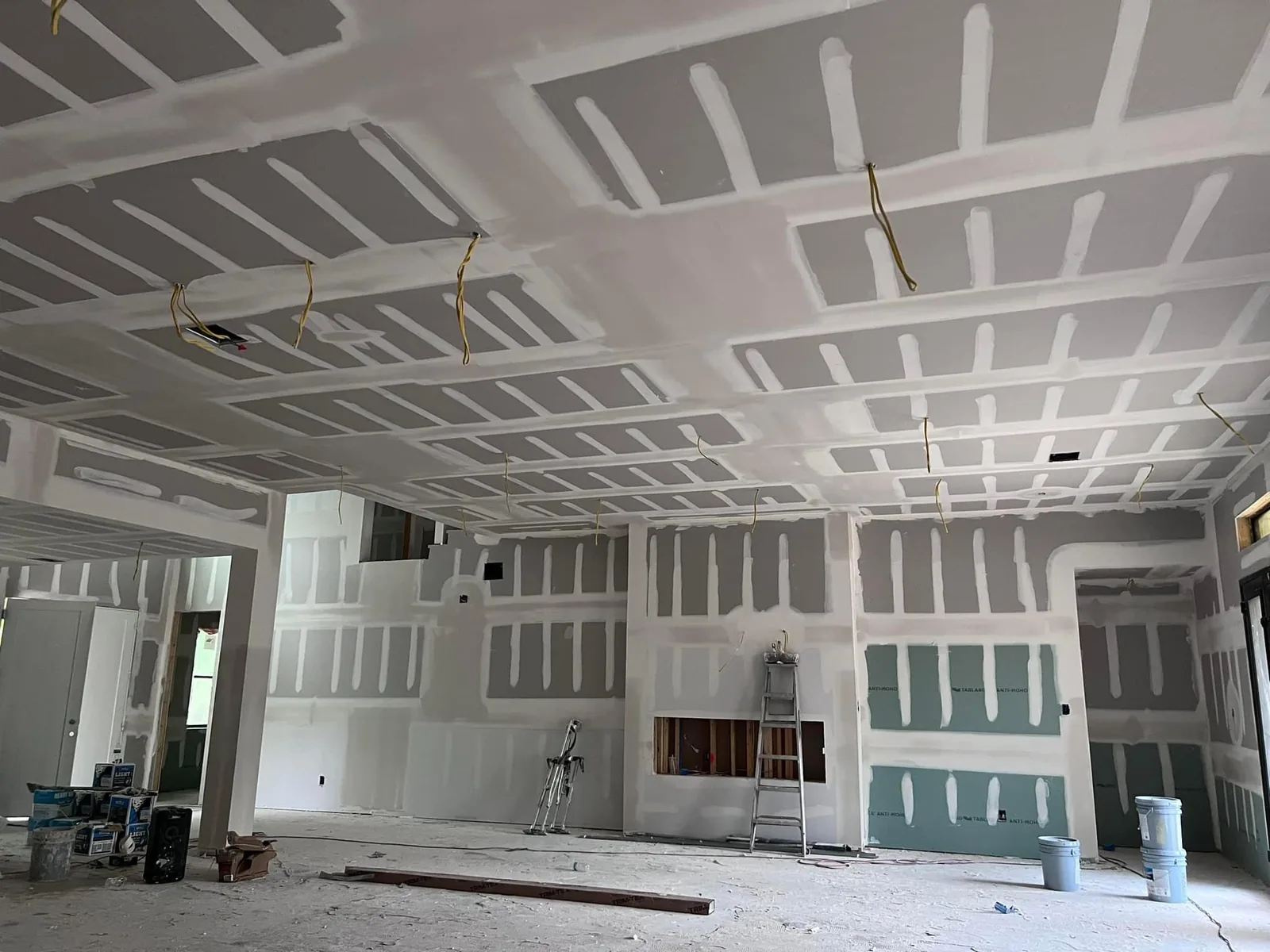 Wide room showing installed drywall panels with taped wall and ceiling joints